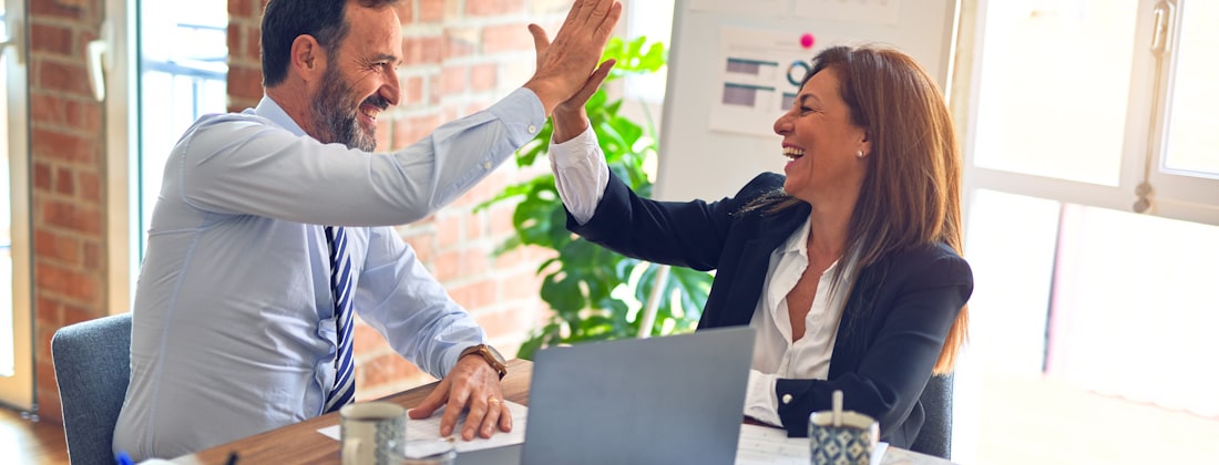 Two colleagues celebrating at a desk in an office