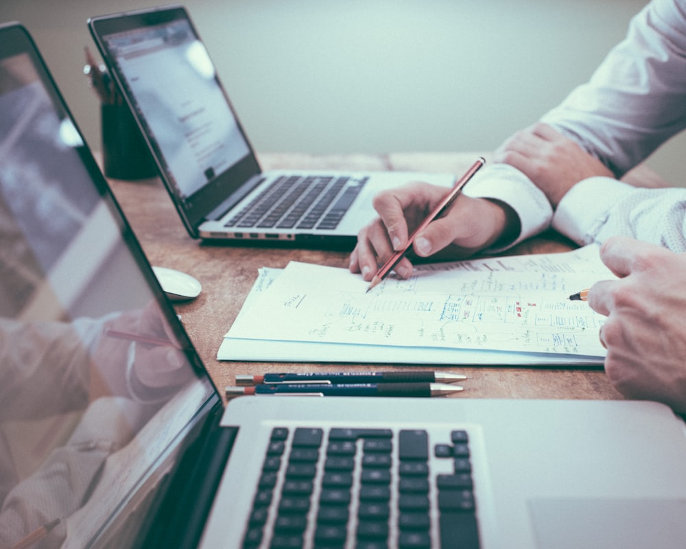 Two people working through paperwork and laptops at a desk