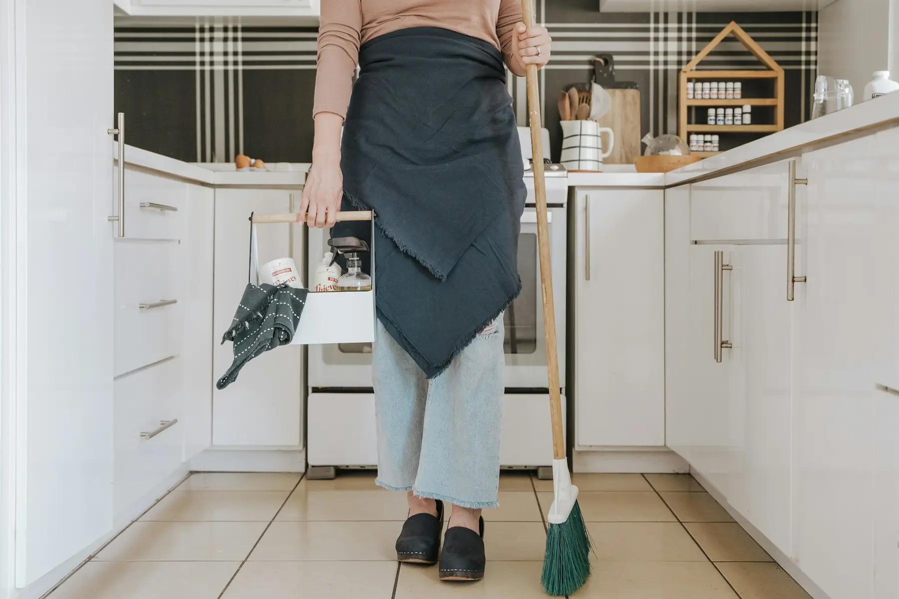 A cleaner with a caddy and broom in a bright white kitchen