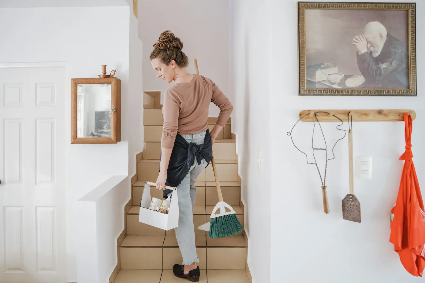 A cleaner carrying a caddy and broom up a staircase