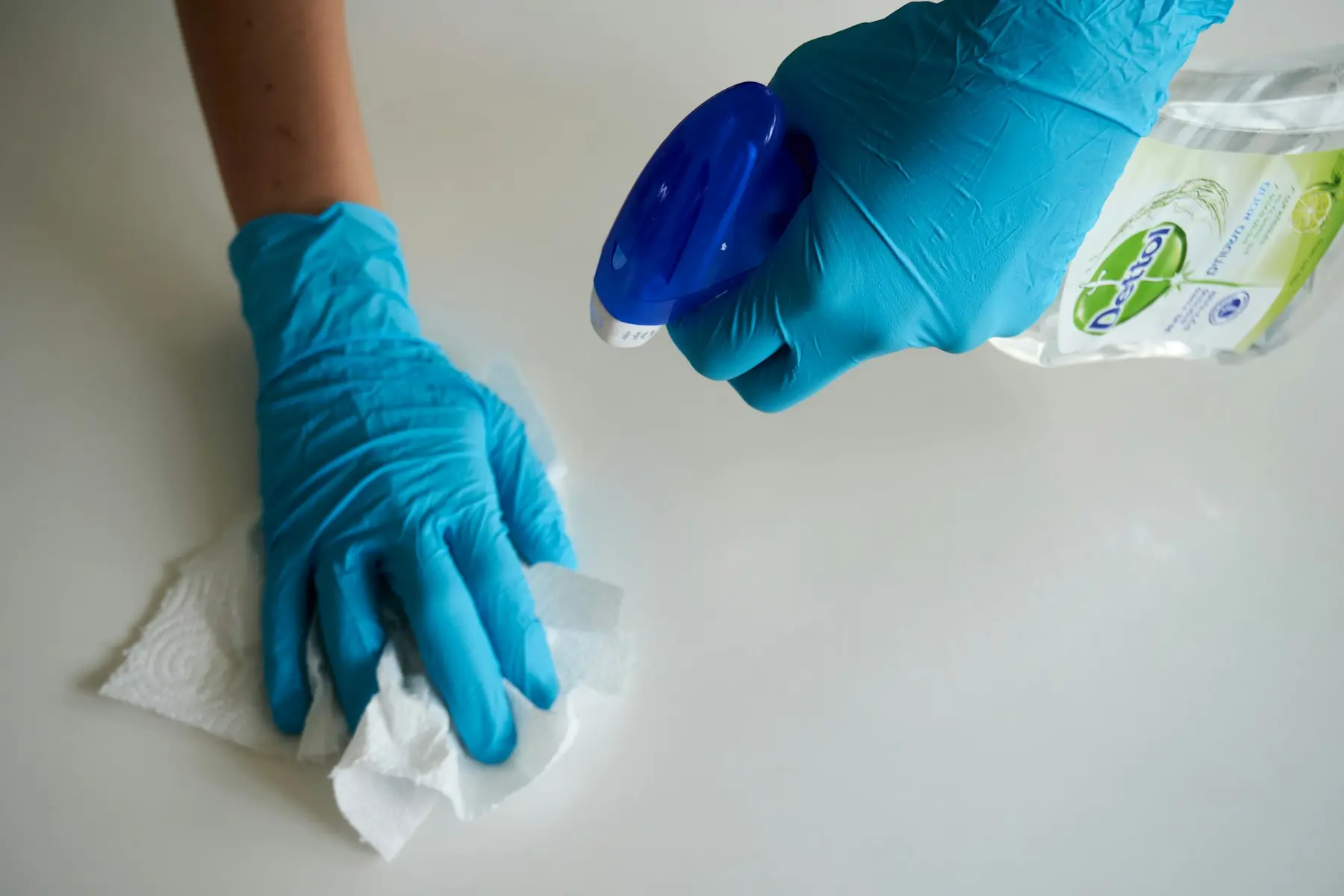 Gloved hands spraying and wiping a white worktop