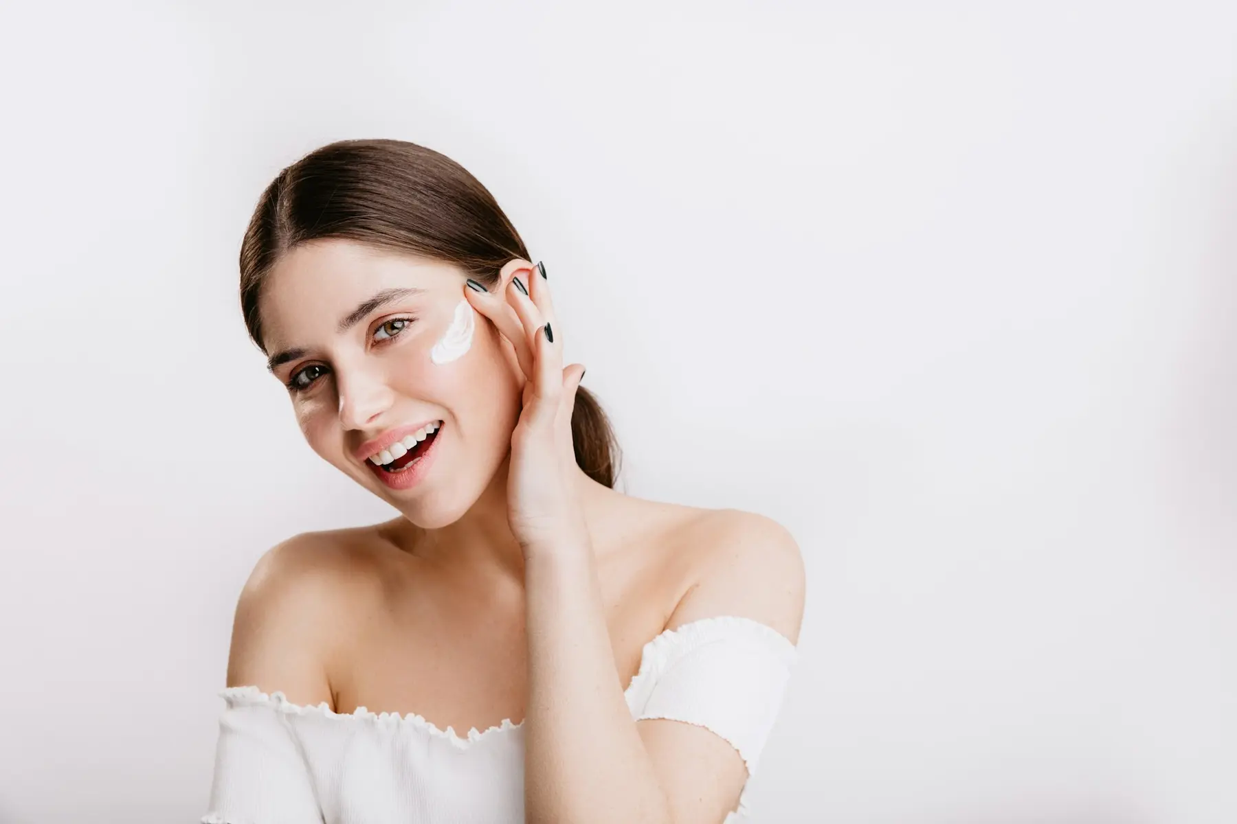 A smiling woman applying a dab of cream to her cheek