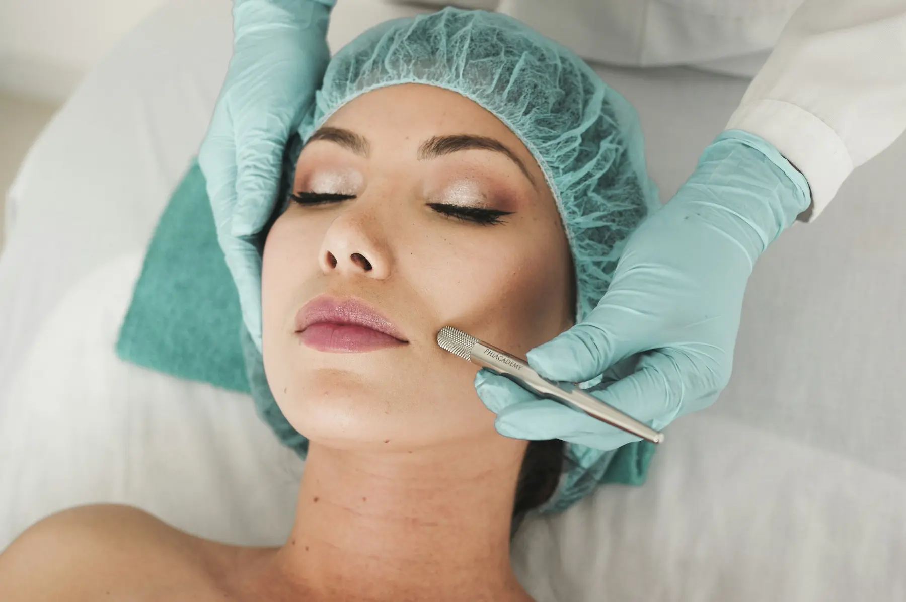 A practitioner in mint gloves dermaplaning a relaxed client's cheek