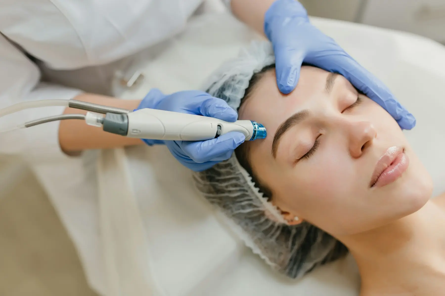 A practitioner in blue gloves using a handheld hydrating device on a client's forehead