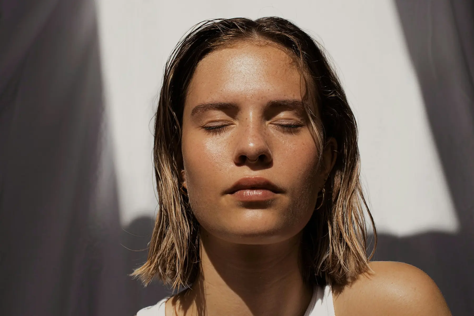 A woman with wet hair and bare skin, eyes closed in soft sunlight