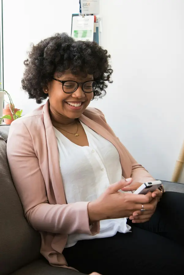 A smiling woman in glasses reading a message on her phone